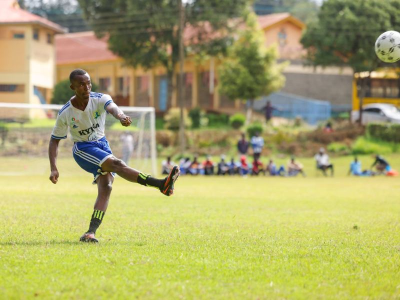 A footballer in white county kit strikes the ball as spectators watch from the touchline