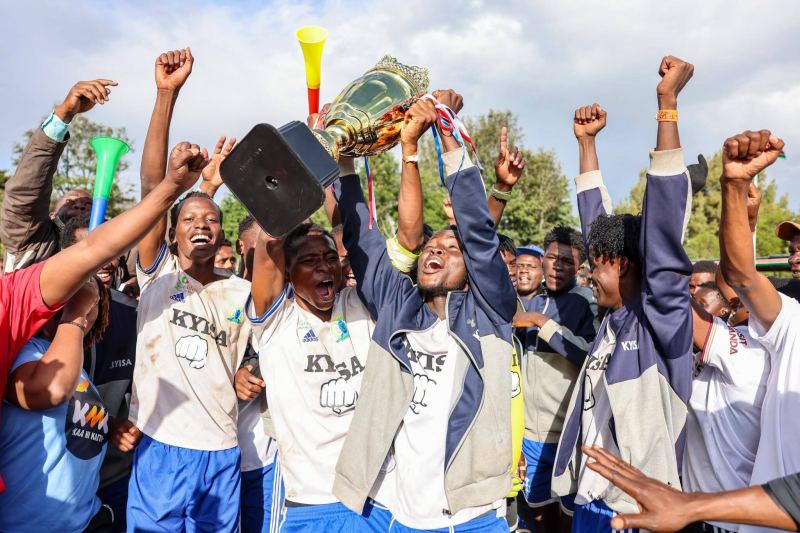 Makueni players lift the championship trophy with fists and vuvuzelas raised in celebration